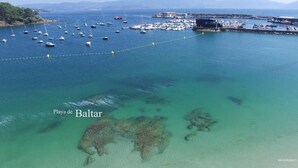 An aerial view of Playa de Baltar with clear turquoise waters, boats, and a marina. - Hotel Maracaibo (Sanxenxo)