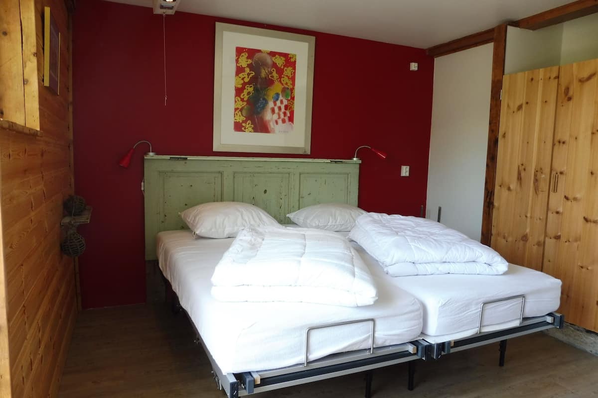 A single-bed room with a green headboard, white bedding, and a red wall with a framed artwork.