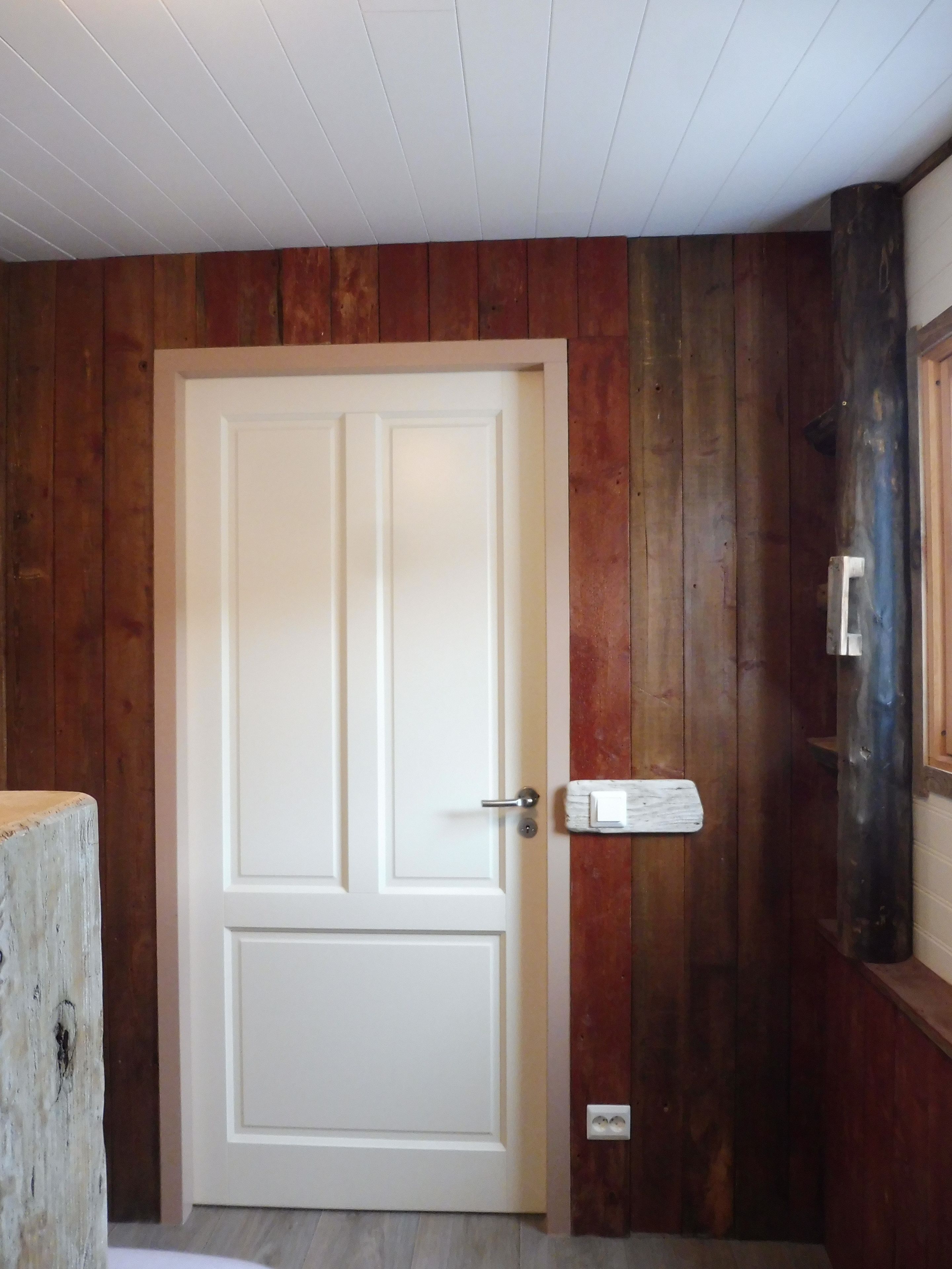 A white door with a handle, set in a wooden wall with a vertical panel design.