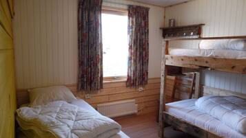 A room with a wooden bunk bed, a single bed, a window with curtains, and a radiator.