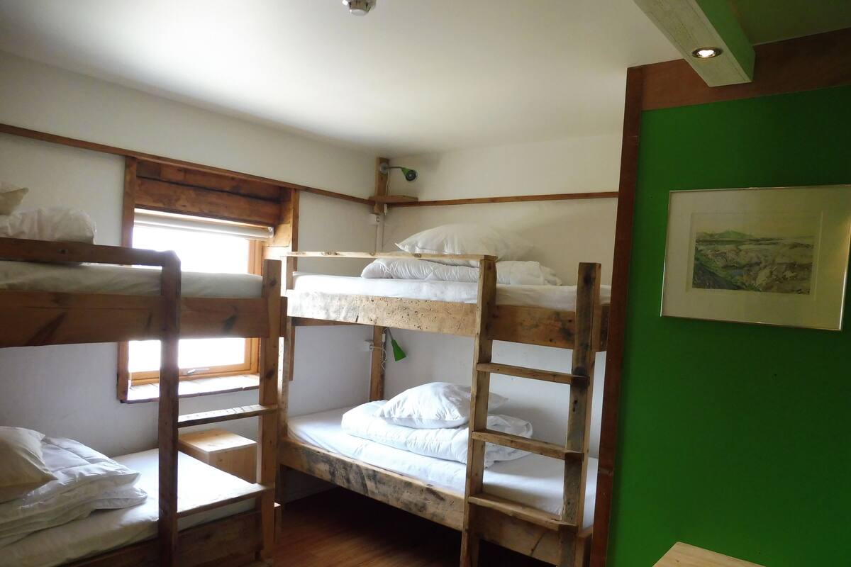 A bunk bed room with wooden frames, a small wooden stool, and a framed picture on the wall.