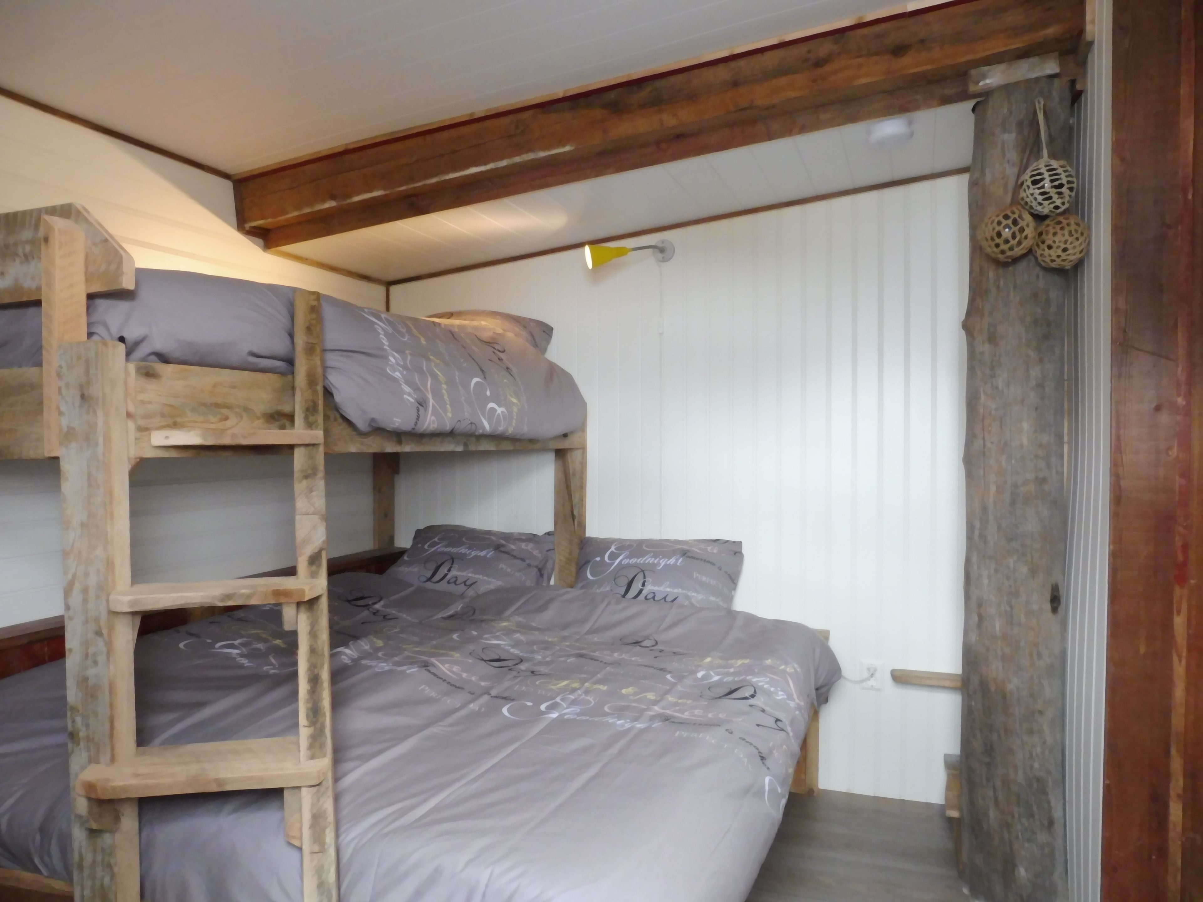 Uma cama beliche com escada, roupa de cama cinza e cabeceira de madeira.