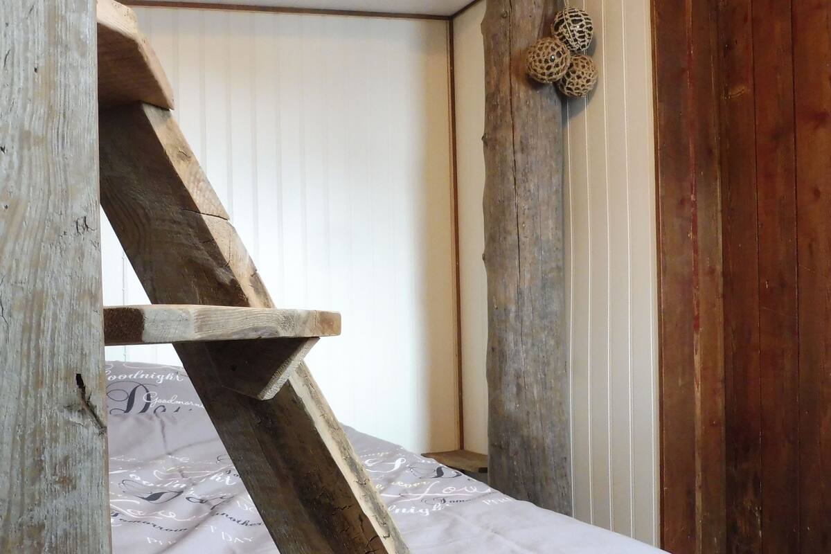 A rustic wooden staircase leading to a bed with a white sheet and a decorative wall hanging.
