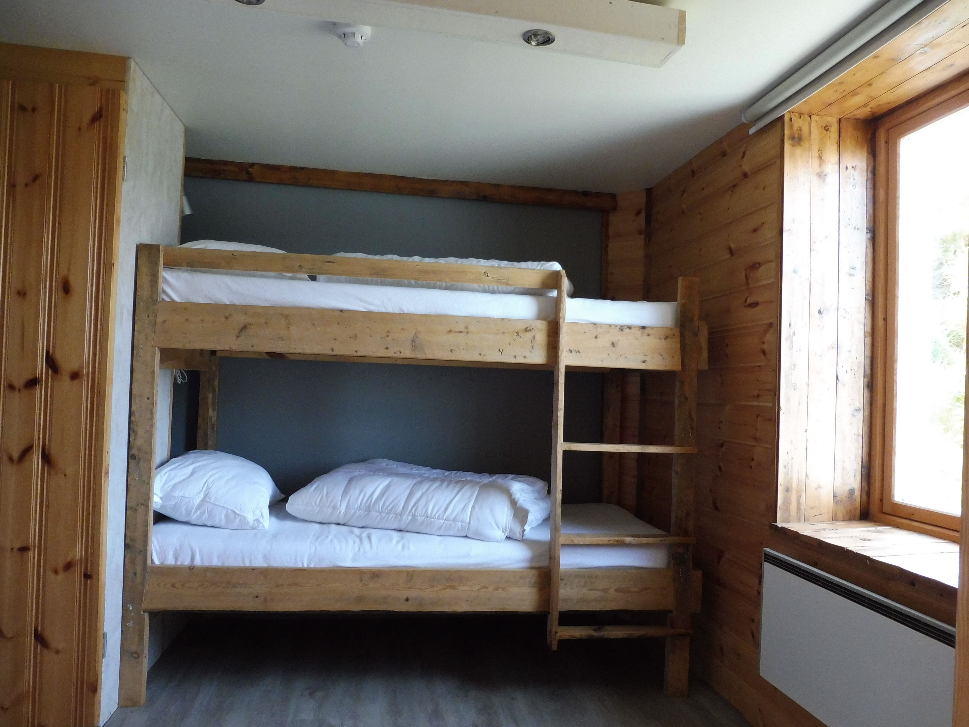 Une chambre avec un lit superposé, des murs en bois et une fenêtre.