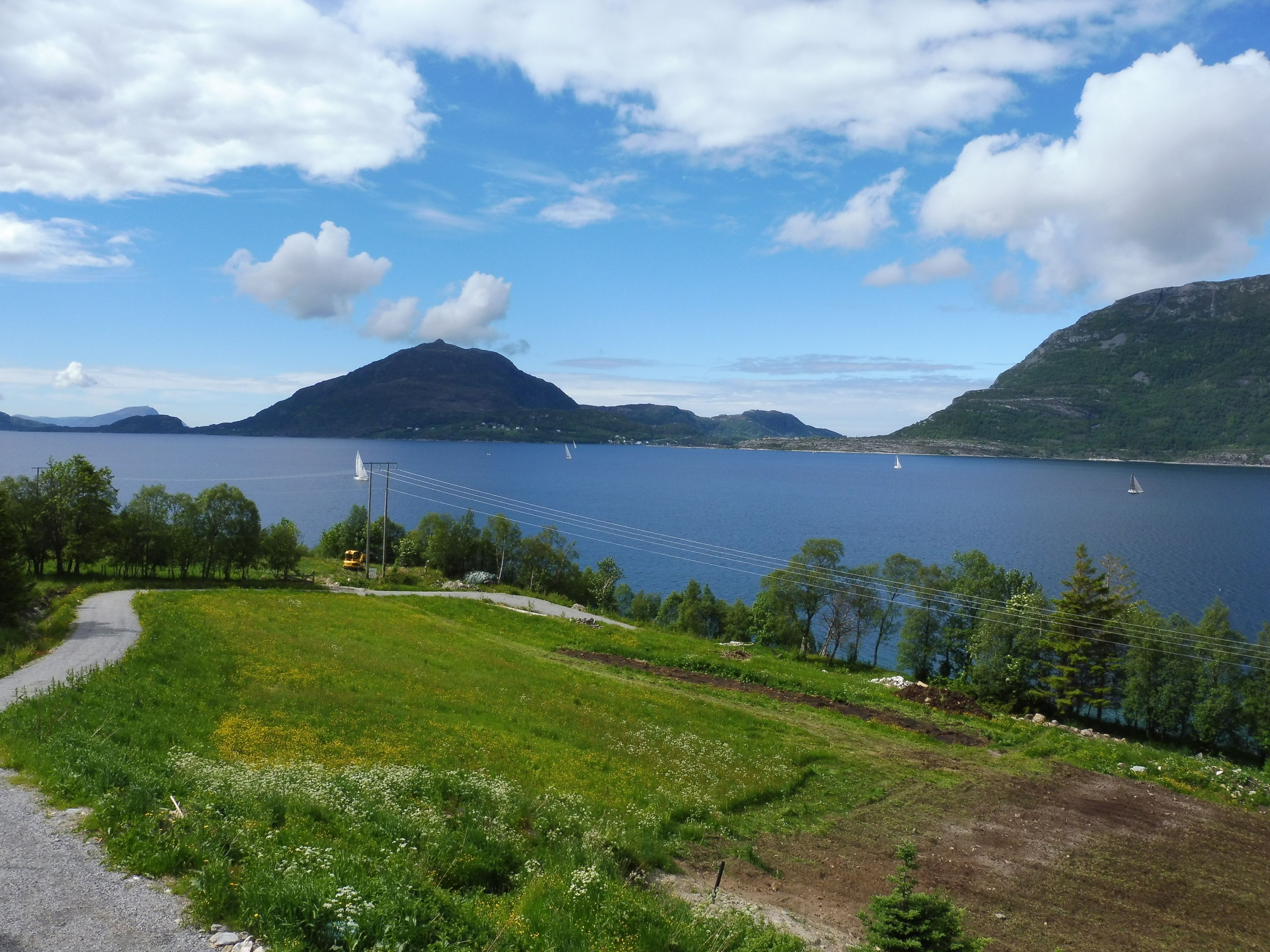 A scenic view of a lake with sailboats, surrounded by lush greenery and mountains.