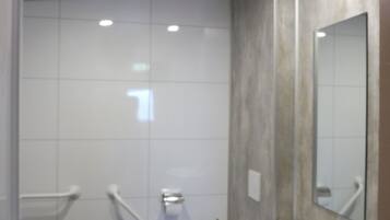 Ein modernes Badezimmer mit weißen Fliesen, einer Toilette, einem Waschbecken und einem Spiegel.