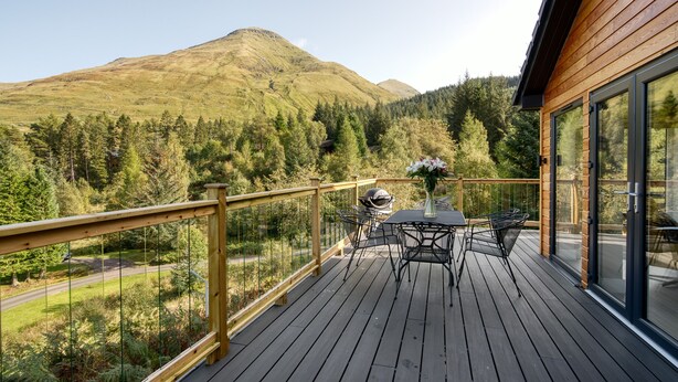 Eine Holzterrasse mit Tisch und Stühlen mit Blick auf ein bewaldetes Tal und Berge.