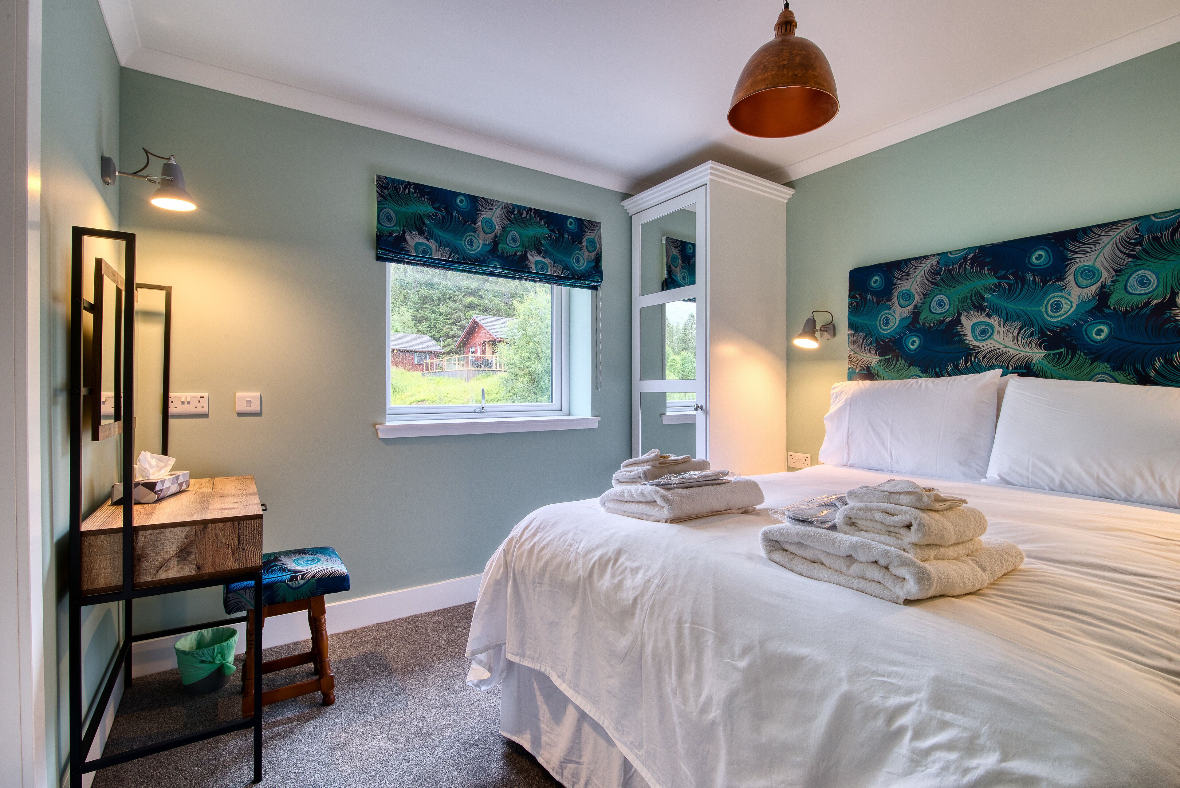 A bedroom with a bed, a desk, a chair, and a window with a view of a house.