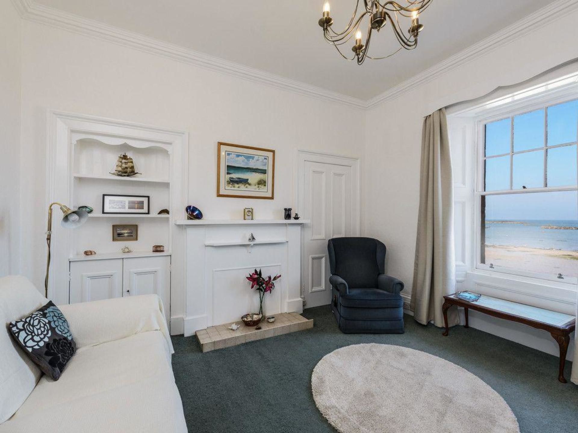 A well-lit room with a fireplace, a comfortable sofa, a chair, and a view of the beach through a large window.