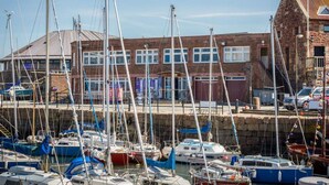 A marina with multiple boats docked, a brick building with windows, and a clear sky.