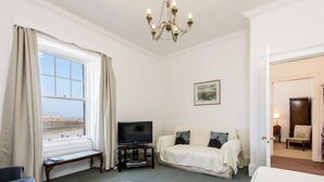 A hotel room with a large window, a TV on a stand, a sofa, a chair, and a bed.