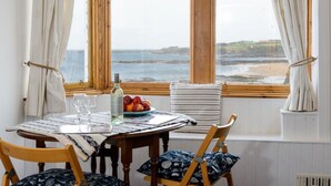 A dining table with a bottle, glasses, and fruit by a window with a view of the sea. - Bass Rock View (North Berwick)