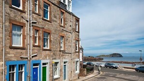 A coastal street with stone buildings, a blue door, and a view of the sea. - Bass Rock View (North Berwick)