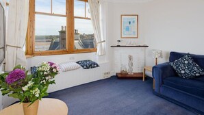 A living room with a blue sofa, a white fireplace, and a large window with curtains. - Bass Rock View (North Berwick)