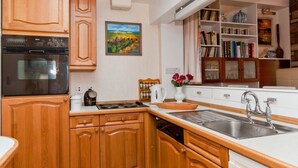 A kitchen with wooden cabinets, a Bosch oven, a coffee machine, a sink, and a bookshelf with books and decorative items. - Greylag Cottage (Gullane)