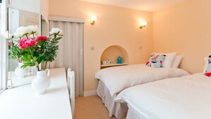 A hotel room with two beds, a small desk, a mirror, and a window with flowers. - Greylag Cottage (Gullane)