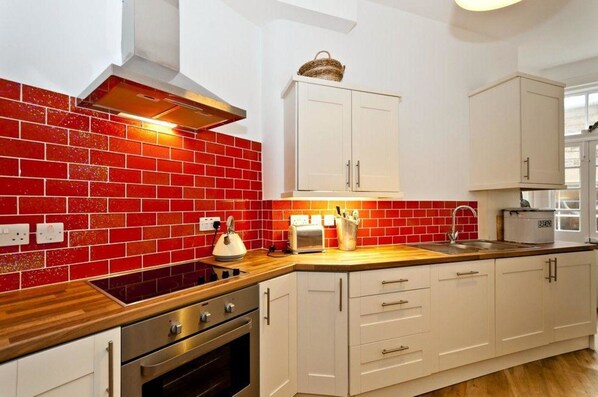A kitchen with red tiled backsplash, white cabinets, a wooden countertop, a built-in oven, and a toaster. - Blue Seas (North Berwick)