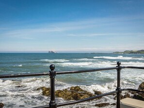 A coastal view with a railing, waves, and a distant island. - Blue Seas (North Berwick)