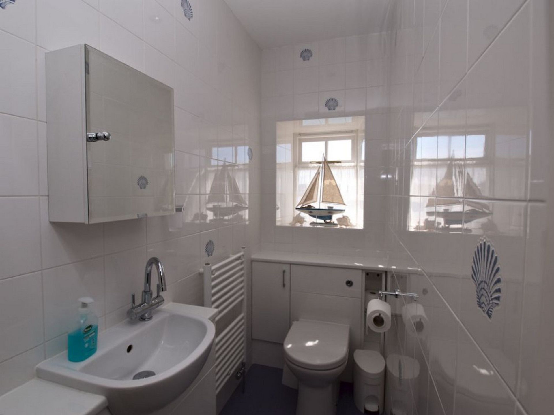 Een badkamer met een wastafel, toilet en raam met een decoratie van een zeilboot.