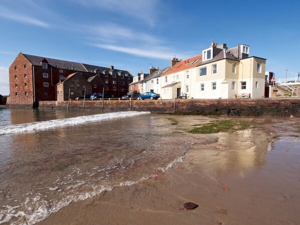 A coastal building with a brick facade and a white upper section, adjacent to a sandy beach with gentle waves.