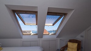 A bedroom with a skylight, a bed, a chair, and a view of the sea. - Quayside Cottage (North Berwick)