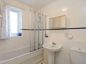 Un baño con bañera, lavabo, inodoro, ventana con cortinas y espejo.