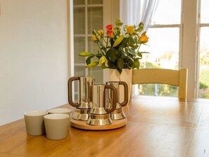 Una mesa de madera con una jarra metálica, un florero y tres tazas blancas.