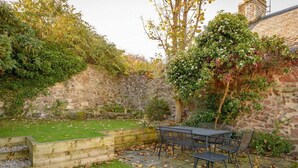 A patio with a table and chairs, surrounded by a stone wall and greenery. - Southcot (North Berwick)