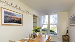 A dining area with a wooden table, chairs, a vase with flowers, and a painting on the wall. - Southcot (North Berwick)