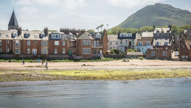 A coastal town with traditional stone buildings, a church, and a hill in the background. - Southcot (North Berwick)
