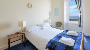 Una habitación de hotel con una cama, un escritorio con lámpara, una silla y una ventana con cortinas.