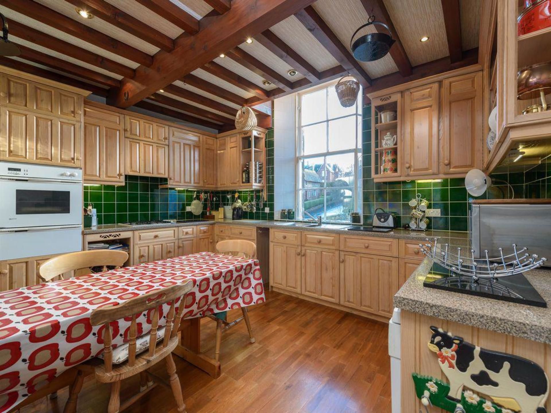 Een keuken met houten kastjes, een eettafel met een tafelkleed met patroon, en een raam dat natuurlijk licht binnenlaat.