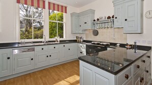 A spacious kitchen with light blue cabinets, a black countertop, and a window with a striped valance. - West Links View (North Berwick)