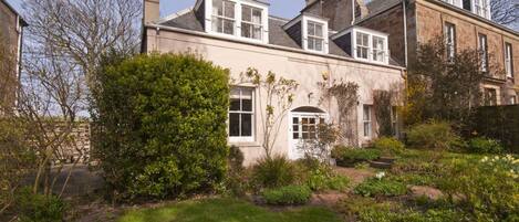 A traditional two-story house with a well-maintained garden, a white door, and multiple chimneys.