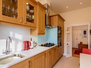 A modern kitchen with wooden cabinets, a stainless steel sink, a red kettle, and a gas stove. - Nungate (North Berwick)