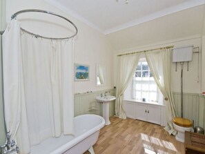 A bathroom with a freestanding bathtub, a sink, a toilet, and a window with curtains. - Nungate (North Berwick)