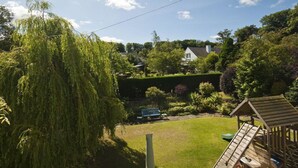 A residential backyard with a wooden playhouse, a lawn, and a variety of trees and shrubs. - Nungate (North Berwick)