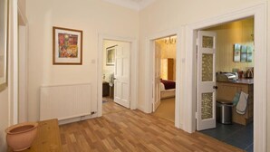 A hallway with wooden flooring, white walls, and a door leading to a room with a bed and a radiator. - Nungate (North Berwick)