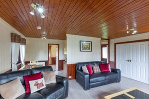 A spacious living area with two black leather sofas, a wooden ceiling, and a white door in the background.