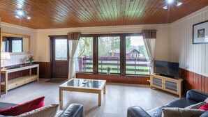 Uma sala de estar ampla com teto de madeira, janelas grandes, televisão e um espaço de estar confortável.