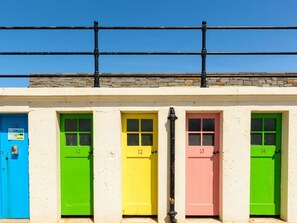 A row of brightly colored doors numbered 10 to 14, with a stone wall and a metal railing above. - Puffin's Nest (North Berwick)
