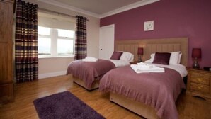 A hotel room with two beds, a wooden floor, and a purple wall. - Rowan Tree Cottage (Cupar)