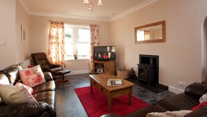 A living room with a sofa, a wooden coffee table, a television, a fireplace, and a mirror on the wall. - Rowan Tree Cottage (Cupar)