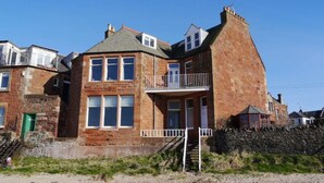 A two-story stone building with a balcony on the upper floor, a green door, and a staircase leading to the entrance. - Seafield (North Berwick)