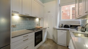 A modern kitchen with white cabinets, a black oven, a built-in microwave, and a window with a view of the outside. - Seafield (North Berwick)