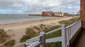 A coastal view with a sandy beach, a white fence, and buildings in the background. - Seafield (North Berwick)
