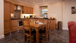 A modern kitchen with wooden cabinets, a dining table, and a window with a view. - Cherry Blossom Cottage (Cupar)