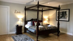 A four-poster bed with a floral bedspread, two bedside tables with lamps, a grey rug, and a framed picture on the wall. - Cherry Blossom Cottage (Cupar)
