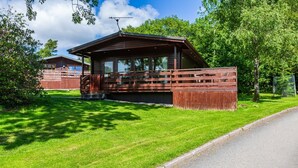 A wooden cabin with a porch, surrounded by a well-maintained lawn and trees. - Bluebell Lodge 2 with Hot Tub (Newton Stewart)