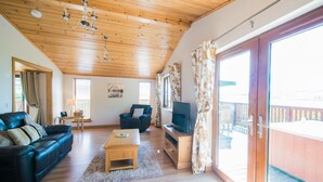 Ein geräumiges Wohnzimmer mit Holzboden, einem schwarzen Ledersofa, einem Couchtisch aus Holz und einem Fernseher auf einem Holzboden.